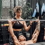 Man lifting weights with woman spotting in Mexico City gym. Urban and dynamic fitness scene.